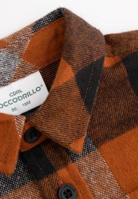 Brązowa i pomarańczowa koszula w kratę z kołnierzykiem zapinanym na guziki, wykonana z tkaniny o fakturowanym splocie, z kontrastującymi czarnymi akcentami.