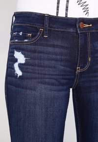 Ciemnoniebieskie dżinsy wykonane z denimu o wąskim kroju, z przetarciami na przedniej kieszeni oraz klasycznym fasonem z pięcioma kieszeniami.