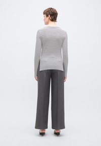 Fekete-fehér csíkos hosszú ujjú felső, szürke bőszárú nadrággal párosítva. A felső lekerekített nyakkivágással és enyhén ívelt alsó szegéllyel rendelkezik.