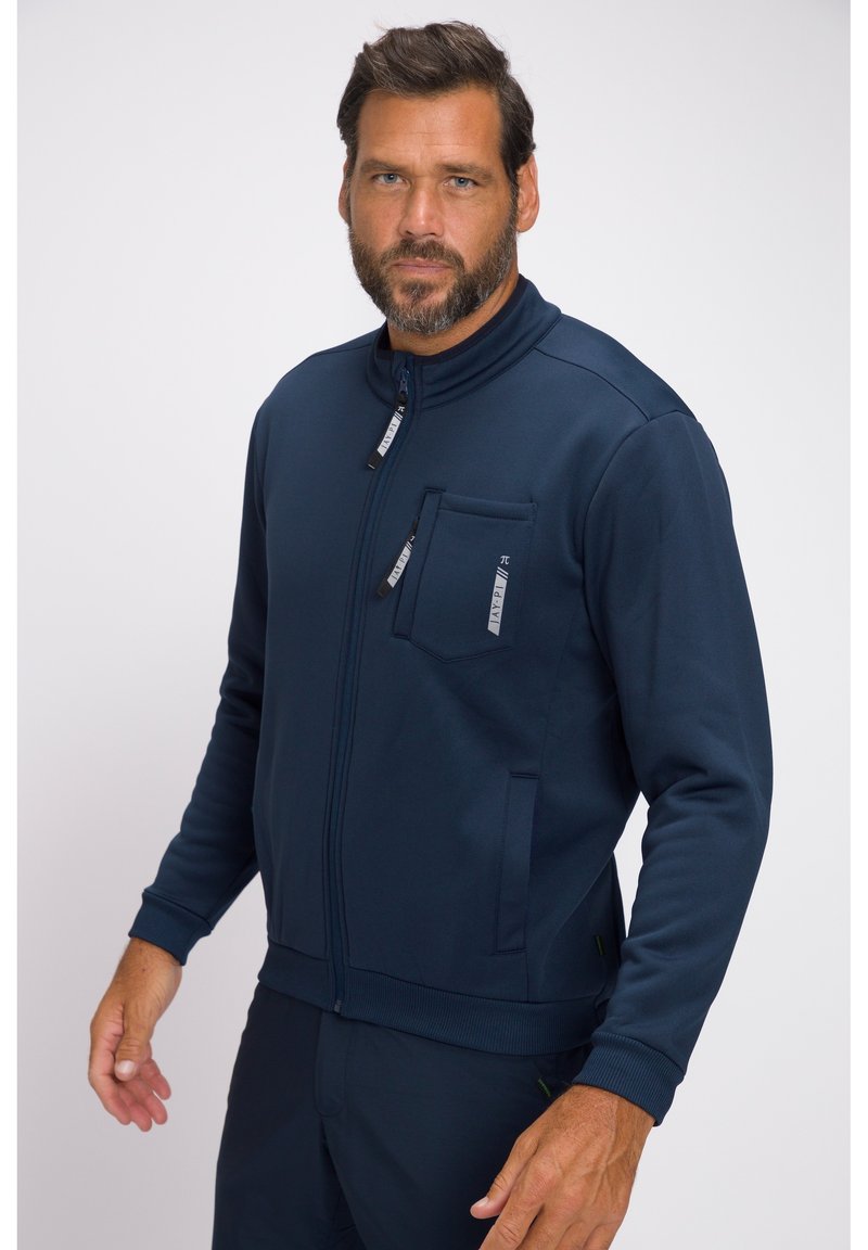 Tummansininen vetoketjullinen takki, joka on valmistettu sileästä kankaasta. Ominaisuuksiin kuuluvat korkea kaulukset, vetoketjulla varustettu rintatasku, sivutaskut ja ribbikantit.