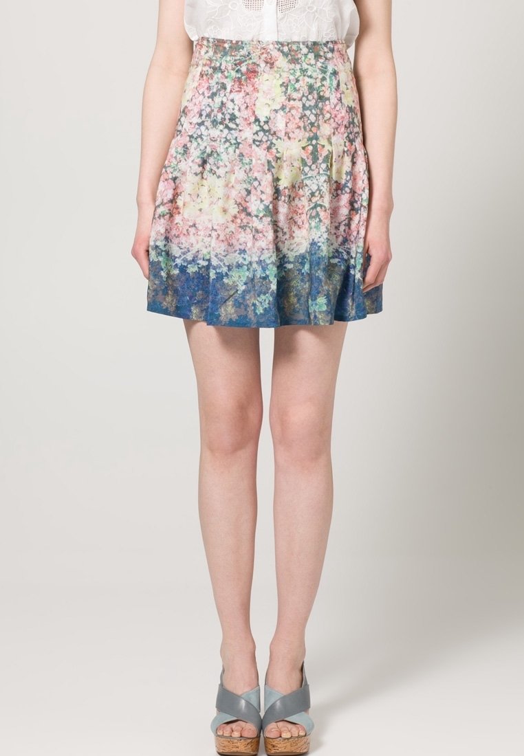 Jupe à motifs floraux dans des teintes pastel, présentant des plis et un dégradé allant du rose au bleu. Fabriquée en tissu léger, elle arrive au-dessus du genou.