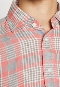 Röd och grå rutig skjorta, knäppning med krage, lättviktigt tyg, synliga knappar och en strukturerad väv med varierande randbredder.