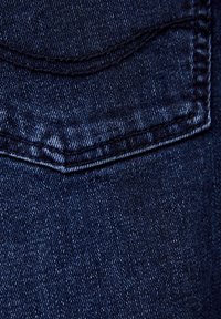 Mörkblå denimtyg med en strukturerad väv, synliga sömmar och en liten fickdetalj.