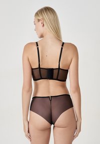 Set di lingerie trasparente nera composto da reggiseno con chiusura posteriore e mutandine a vita alta, con una texture liscia e senza motivi o accenti visibili.