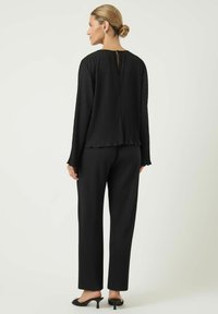 Svart ribbestrikket bluse med detalj i ryggåpningen, kombinert med matchende ribbestrikkede bukser. Jevn tekstur, avslappet passform og lange ermer.