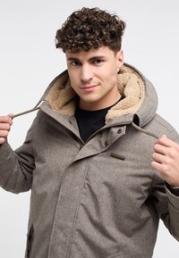 Brun texturerad jacka med fuskpälsfoder på huvan. Har dragkedjestängning, justerbara dragsko och sidofickor.