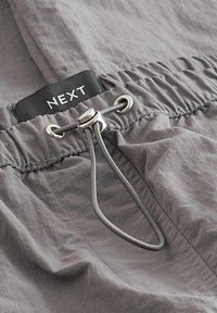Grå letvægts shorts med elastisk talje, featuring en snor og sølvfarvet hardware. En sort etiket med "NEXT" er synlig.