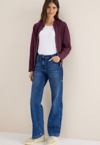 Chaqueta burdeos con cremallera y camiseta blanca combinadas con jeans de pierna ancha azules y zapatillas beige, con un ajuste casual y relajado.