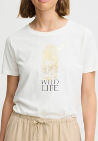 T-shirt en coton blanc avec un graphique de tigre en feuille d'or et le texte "WILD LIFE" en noir, col rond et manches courtes.