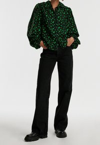 Blusa nera a fiori con motivi verdi, design con bottoni, maniche a palloncino; abbinata a jeans neri a zampa d'elefante e stivali neri chunky.