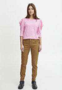 Pink puff-sleeve top with round neckline, paired with slim-fit, light brown pants featuring five buttons and black ankle boots.