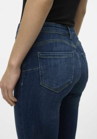 Jeans de mezclilla azul oscuro con un diseño ajustado, bolsillos traseros con costuras decorativas y una textura suave.