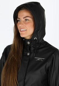 Svart vattentät jacka med huva, tryckknappar och dragsko. Har en 'SWEDEMOUNT'-logotyp och en glänsande yta.