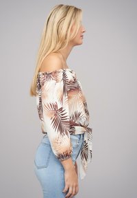 Blusa de hombros al descubierto en tejido ligero con patrones de hojas en marrón y crema. Presenta un lazo en la cintura y mangas abombadas.