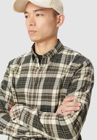 Karierte Button-Down-Bluse in Beige, Braun und Grün. Mit einem kragenlosen Ausschnitt und langen Ärmeln mit geknöpften Manschetten. Texturiert.