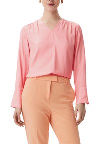 Rosa Bluse mit langen Ärmeln und V-Ausschnitt. Verfügt über geraffte Details an den Schultern und wird mit peachfarbenen, taillierten Hosen kombiniert. Glattes, leichtes Material.