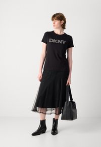 Črna majica s kratkimi rokavi z belo teksturirano "DKNY" blagovno znamko, v kombinaciji s črno slojeno mrežasto krilo, črnimi gležnjarji in črno torbo.
