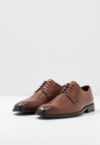 Chaussures habillées en cuir marron avec une finition lisse, bout rond et un design à lacets avec six œillets. Un petit talon empilé finalise le look structuré.