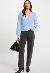 Cárdigan de punto azul claro con escote en V, cierres de botones y patrón texturizado, combinado con jeans negros de cintura alta y botas de tacón negro.