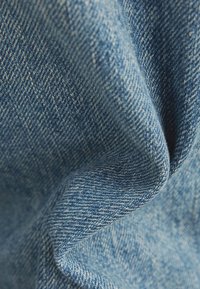 Blå denimtyg med en strukturerad yta, som har ett klassiskt vävmönster och mjuk finish. Materialet verkar lätt och flexibelt.