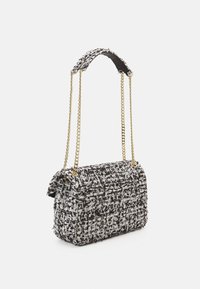 Sac à main en tweed noir et blanc avec une texture matelassée, des anses en chaîne dorée et une fermeture à rabat. Forme rectangulaire compacte avec un design structuré.
