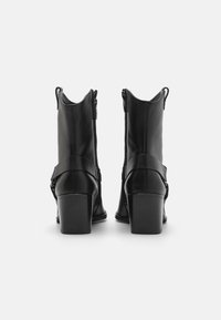 Black leather ankle boots with a stacked heel, side zippers, and a strap detail. Smooth texture and curved collar design.