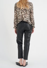 Pantaloni in pelle nera con una vestibilità sartoriale, caratterizzati da una texture liscia e due tasche posteriori, abbinati a una blusa con motivo.
