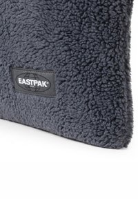 Pocchetto grigio in pile con superficie testurizzata, dotato di un'etichetta nera del logo Eastpak su un lato.