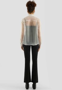 Transparante, lichtbeige button-up blouse met lange mouwen, over een donkergrijze tanktop gedragen, gecombineerd met zwarte flared broek en platform schoenen.