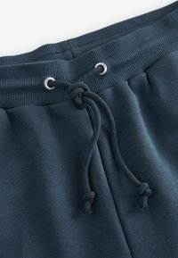 Pantalonii de trening bleu marin au o talie cu nervuri, cu șnur, gromete argintii și o textură moale a materialului.