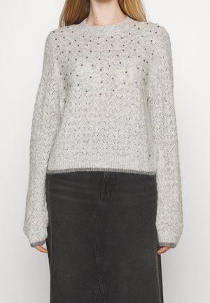Light gray knit sweater with a textured pattern and decorative beads, featuring long sleeves and a ribbed hem. Worn with a black skirt.