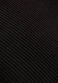 Tissu noir côtelé avec une surface texturée, présentant des rayures verticales régulièrement espacées. Le matériau semble doux et élastique.