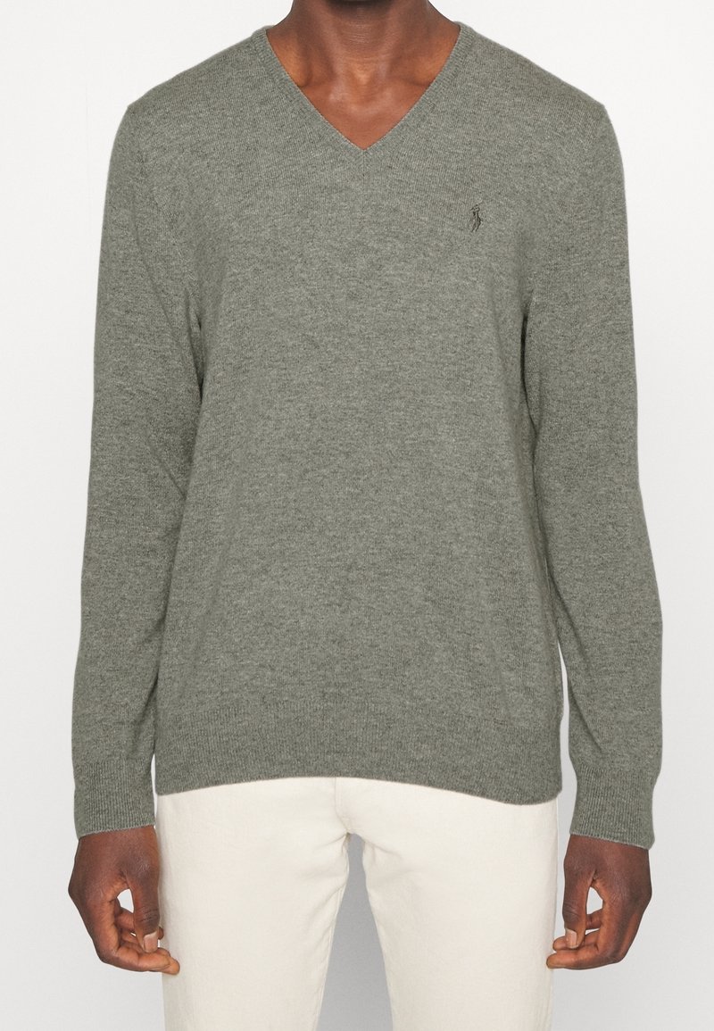 V-ringad tröja i olivgrön ullblandning, med långa ärmar, ribbad nederkant och en diskret logotyp på bröstet. Mjuk textur och åtsittande design.