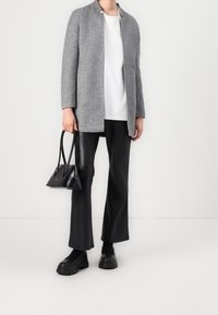 Blazer de punto gris, camiseta blanca, pantalones de cuero negros y zapatos de plataforma negros y gruesos. Sosteniendo un pequeño bolso negro con doble asa.