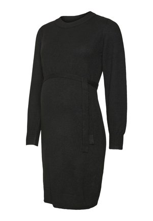 Donna incinta che indossa un vestito nero a maniche lunghe con una vita annodata, che tiene la pancia con entrambe le mani e indossa un braccialetto d'oro.
