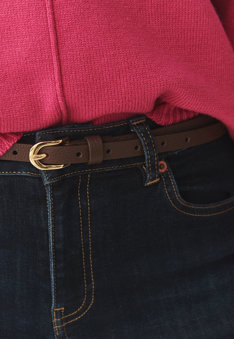 Ceinture en cuir marron avec boucle dorée attachée autour d'un jean bleu foncé, associée à un pull tricoté rose vif rentré dedans.
