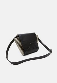 Olkalaukku mustalla sileällä nahkalla varustetulla läpällä, ruudullisella kudotulla pinnalla, jossa on kermaa ja mustaa, säädettävä hihna ja jämäkkä muoto.