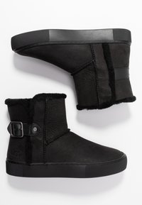 Bottes noires en cuir texturé avec une doublure en peau de mouton. Elles présentent un détail de boucle et une semelle en caoutchouc épaisse. Design hauteur cheville.