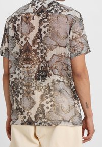 Camicia a maniche corte con una stampa ornata e tenue in tonalità di beige, marrone e grigio, dotata di un colletto classico e una vestibilità comoda.