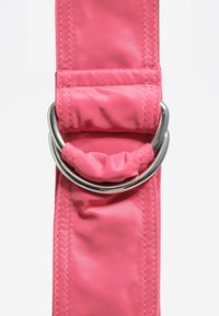 Różowy nylonowy pasek z srebrnym metalowym pierścieniem i marszczonym detalem tkaniny. Gładka tekstura z widocznym szwem. Zbliżenie.