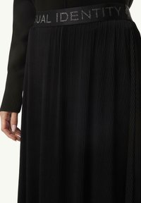 Black pleated skirt with a textured finish, featuring a wide elastic waistband embroidered with "DUAL IDENTITY" in silver.
