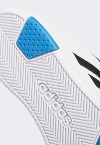 Bijela atletska potplat s ribljom kostom, s plavim gumiranim akcentom i crnim brendiranjem. Tekstura osigurava prianjanje i potporu.