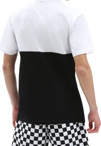 Persona que lleva una camiseta de manga corta con la parte superior blanca y la parte inferior negra, combinada con unos pantalones cortos de cuadros en blanco y negro.