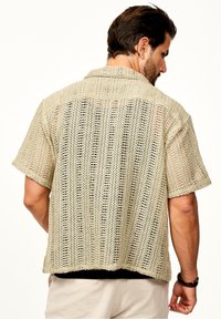 Beige gestricktes Kurzarmhemd mit offener Webstruktur, flachem Kragen und geradem Saum. Das strukturierte Material vermittelt ein leichtes Design.