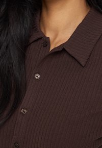 Brown ribbed button-up shirt with a textured fabric, featuring a classic collar and dark buttons. Close-up view of the neckline and collar.