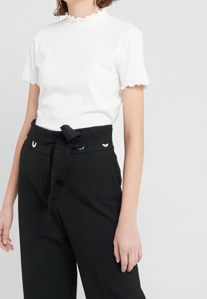 Bílý žebrovaný krátký rukáv se volánovým límečkem, kombinovaný s černými kalhotami s vysokým pasem, které mají texturovaný pásek a kovové detaily.