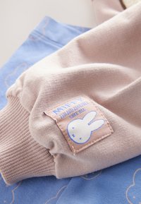 Pull med mjuka beige ärmar som har en tygskylt med en blå tecknad kanin. Den blå kroppstyget visar ett subtilt molnmönster.