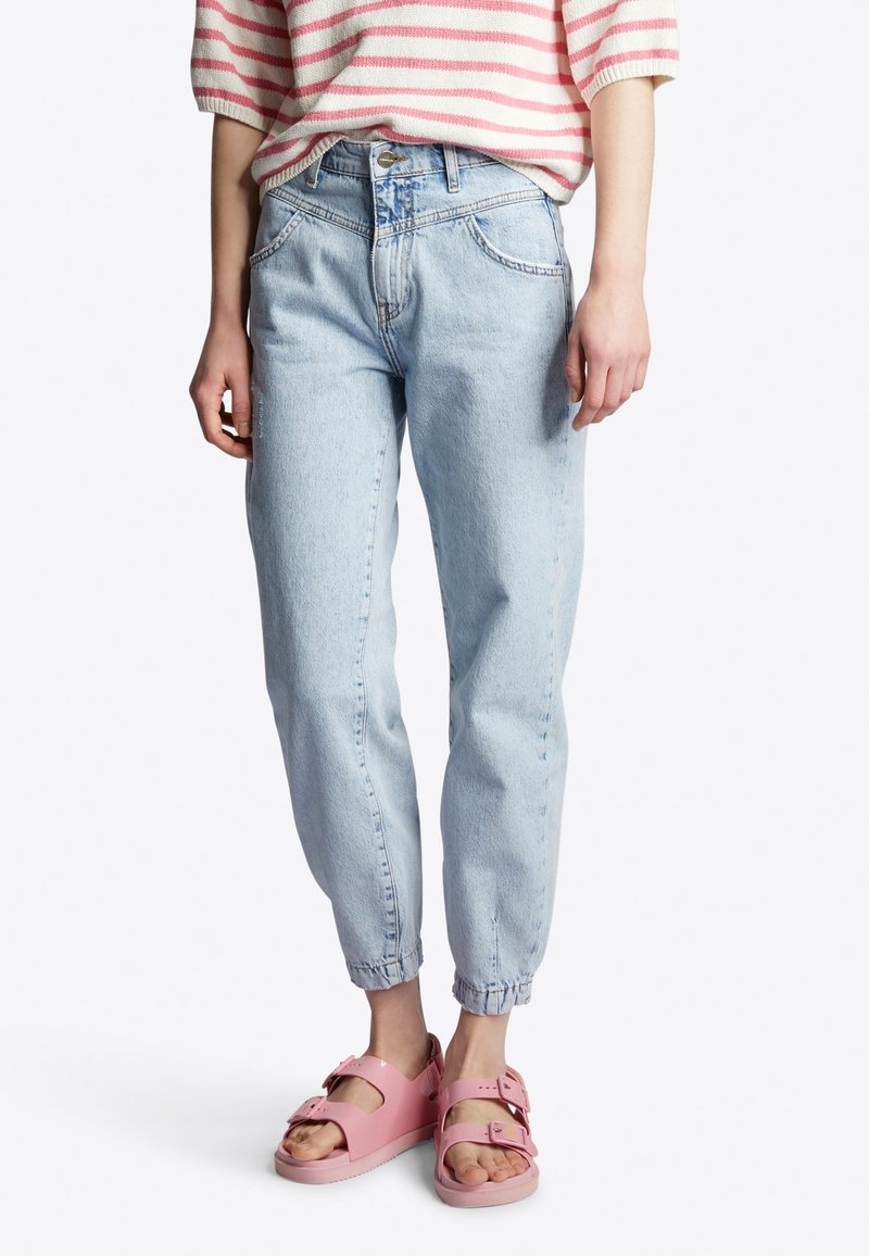 Lichtblauwe denim jeans met taps toelopende pijpen en omgeslagen hemden, gecombineerd met roze rubberen sandalen met verstelbare banden en gespen.