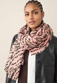 Fular roz cu un model de leopard. Fabricat dintr-un material moale, are margini desfăcute și este împăturit în jurul gâtului, fiind suprapus peste o jachetă neagră.