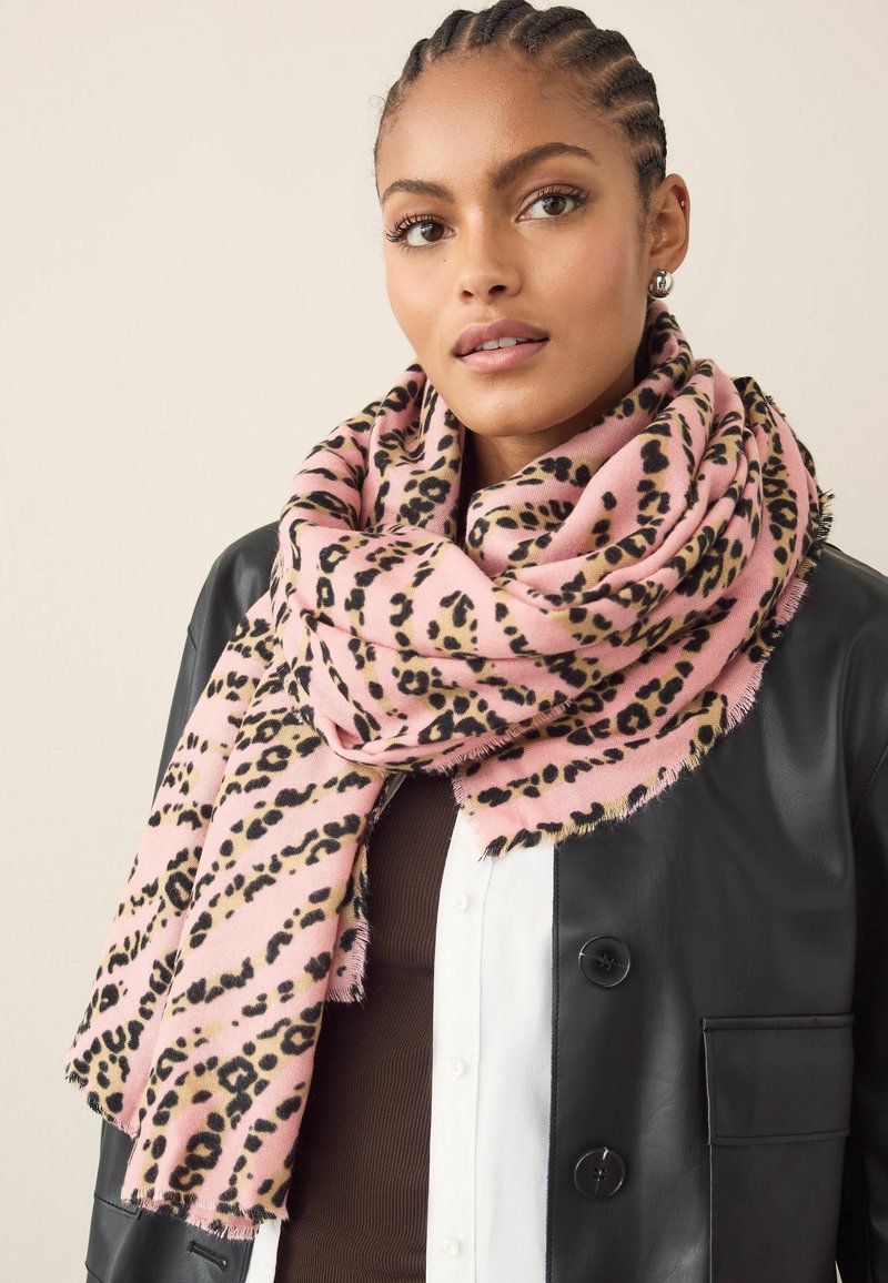 Fular roz cu un model de leopard. Fabricat dintr-un material moale, are margini desfăcute și este împăturit în jurul gâtului, fiind suprapus peste o jachetă neagră.